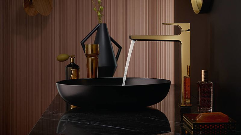 Černé umyvadlo hezky ladí s designovou vodovodní baterií ve zlaté barvě. Fotografie: Hansgrohe